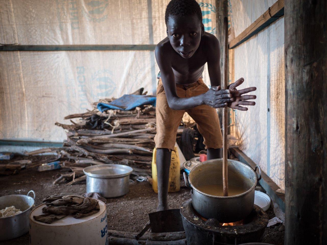 Flüchtlingsjunge aus dem Südsudan bereitet Maisbrei zu (Credit: Aktion Deutschland Hilft /Roland Brockmann)